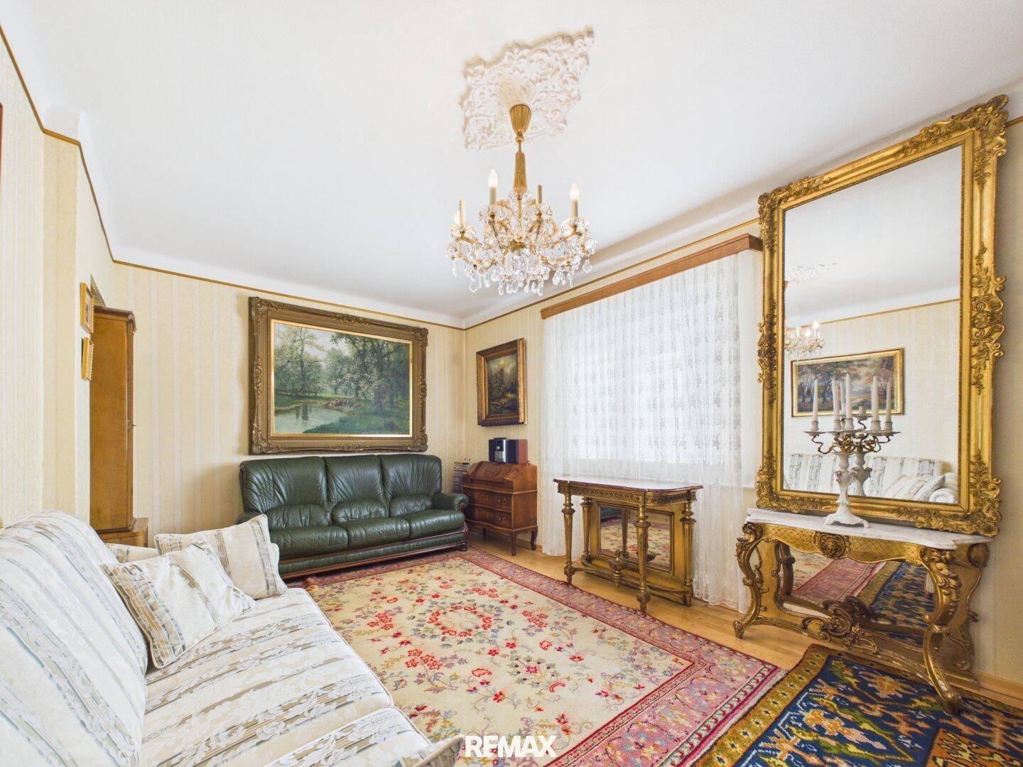 Klassisches Wohnzimmer mit opulentem Goldspiegel, Kronleuchter und traditionellen Möbeln.