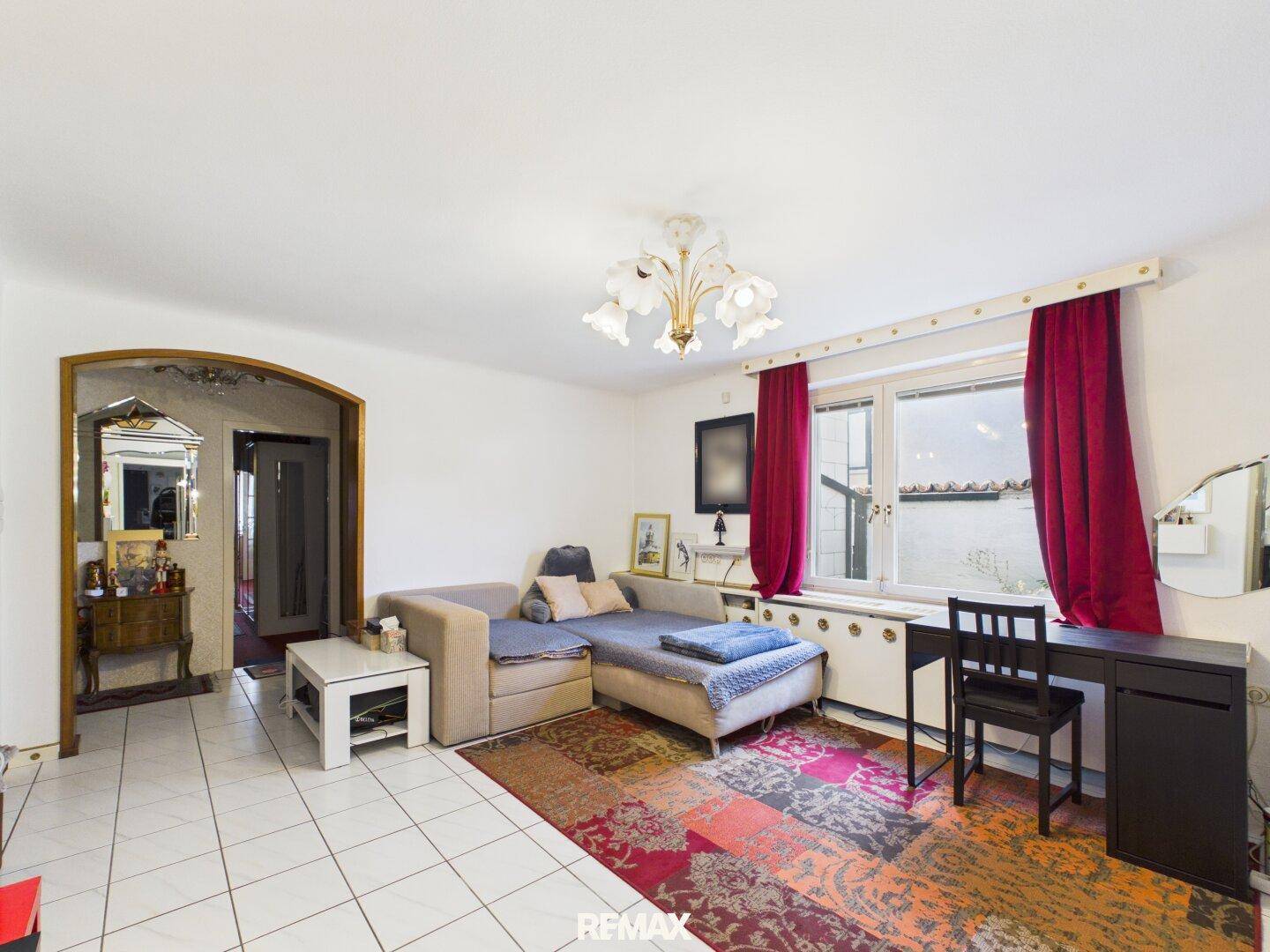 Helles Wohnzimmer mit weißen Fliesen, bequemer Couch und farbenfrohem Teppich.