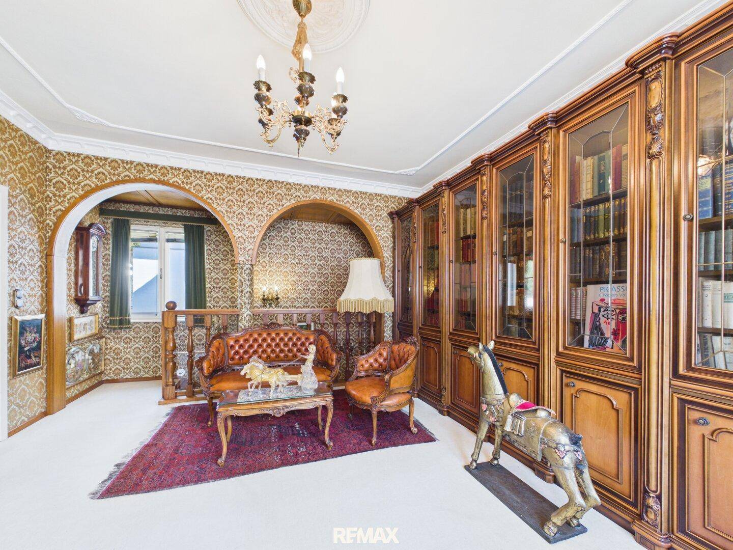 Elegantes Wohnzimmer mit reich verzierten Holzschränken, Ledermöbeln und gemusterter Tapete.