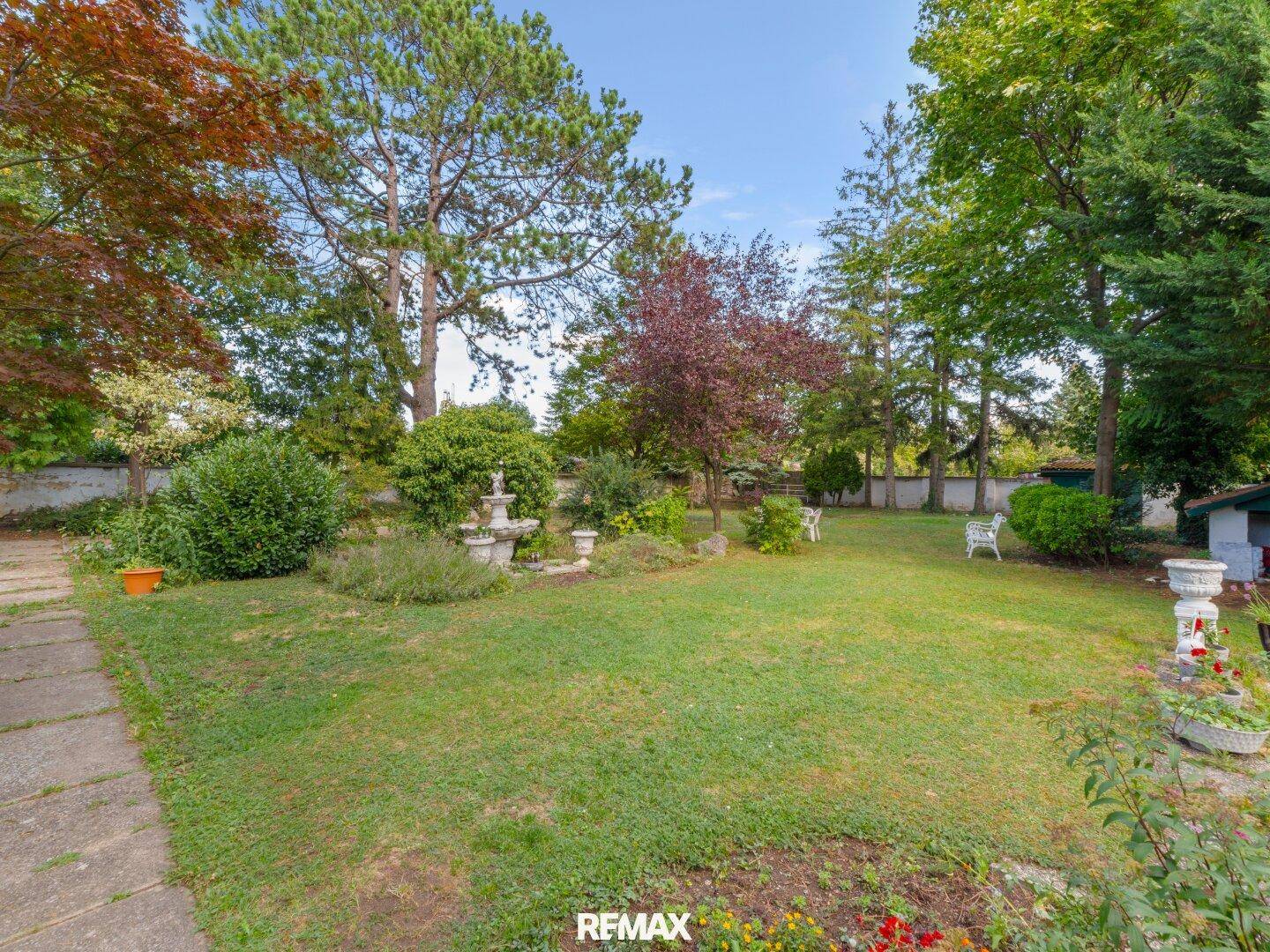 Gepflegter Garten mit Rasenfläche, Bäumen und einem dekorativen Brunnen, ideal zum Entspannen.