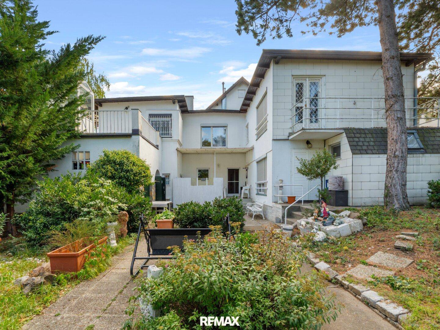 Rückseite des Hauses mit kleinem Gartenbereich, Sitzgelegenheiten und Balkonen.