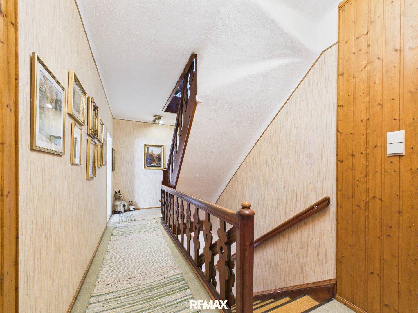 Flur mit Holztreppe, Holzvertäfelung und gemusterter Tapete, die zum Obergeschoss führt.