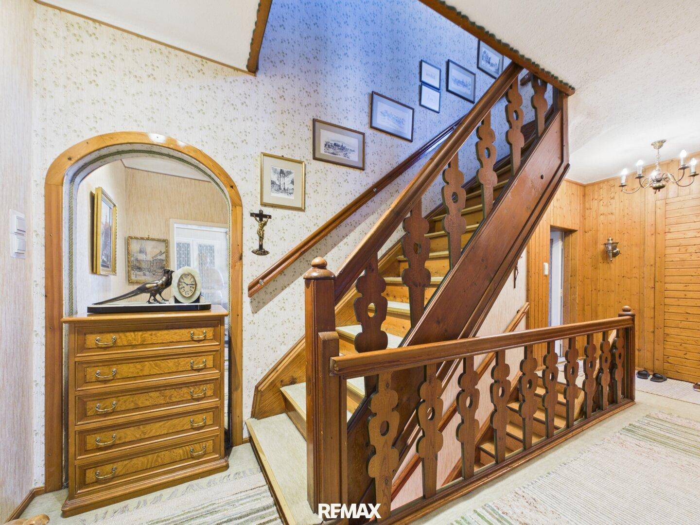 Traditionelles Treppenhaus mit Holzgeländer, gemusterter Tapete und Holzvertäfelung.