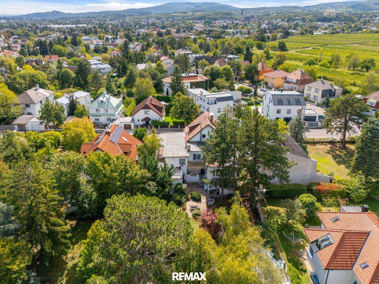 Weitläufige Luftaufnahme der Umgebung mit Häusern, viel Grün und einem Blick auf Weinberge und Berge.