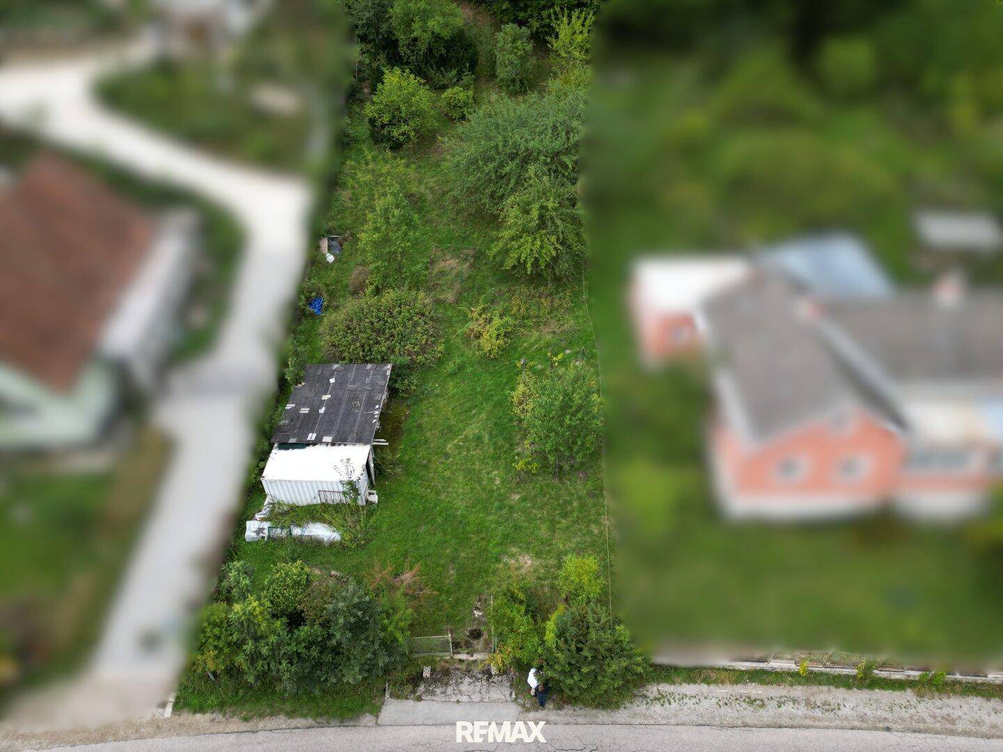 Luftaufnahme eines unbebauten Hanggrundstücks mit dichter Vegetation und einem kleinen Schuppen.