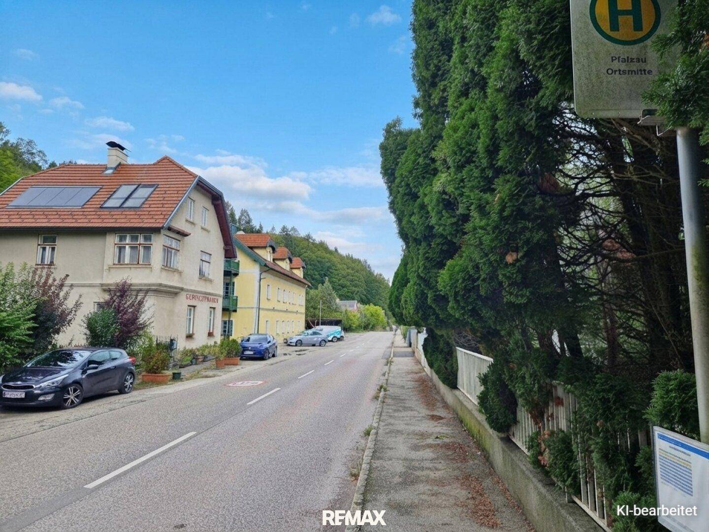 Blick auf eine ländliche Straße mit geparkten Autos, Gebäuden und einer Bushaltestelle.