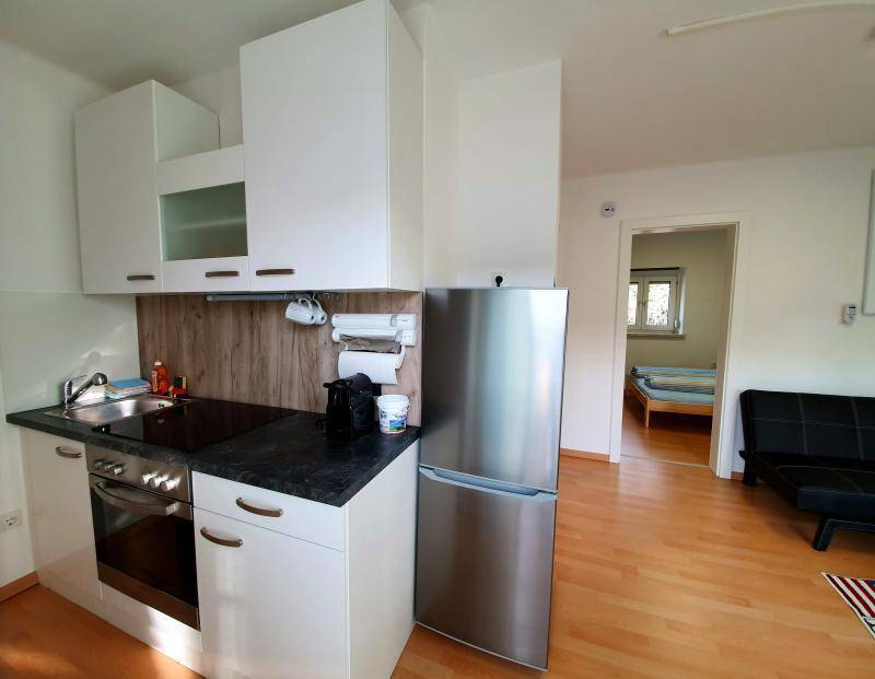 Kompakte Küchenzeile mit Herd, Backofen, Spüle und Kühlschrank, angrenzend an ein Schlafzimmer.