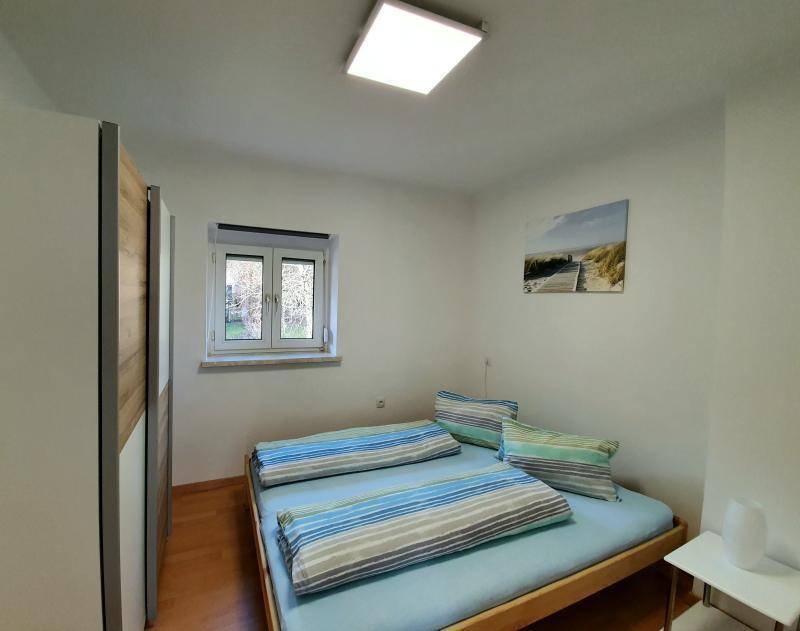 Gemütliches Schlafzimmer mit Doppelbett, Kleiderschrank und einem Fenster mit Blick ins Grüne.
