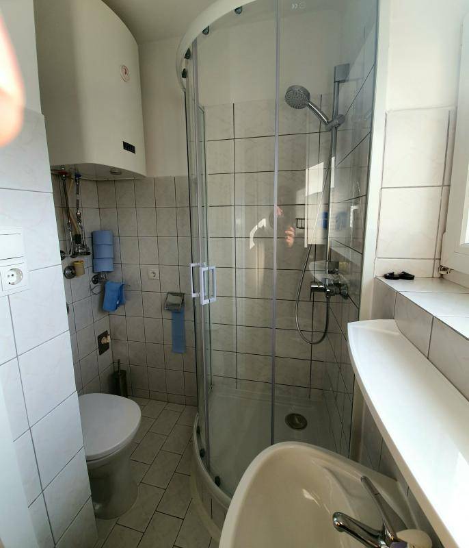 Kleines Badezimmer mit Duschkabine, Toilette, Waschbecken und weißen Fliesen.