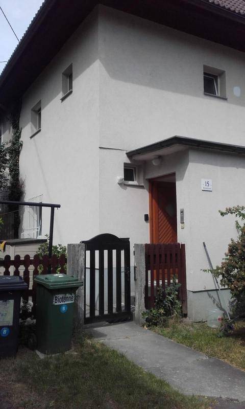 Eingangsbereich des Gebäudes mit Holztor und Mülltonnen, schlichte Fassade.