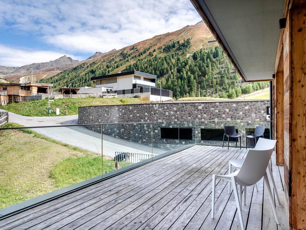 Geräumiger Balkon mit Holzboden und Glasgeländer, bietet einen weiten Blick auf die umliegenden Berge.
