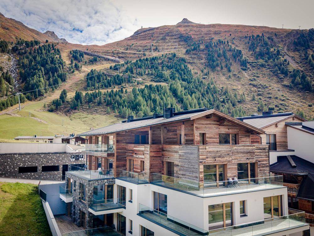 Modernes Gebäude in alpiner Landschaft mit Holz- und Steinfassaden sowie großzügigen Balkonen.