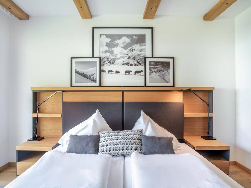 Gemütliches Schlafzimmer mit Holzbalken an der Decke und modernen Nachttischen mit Leselampen.