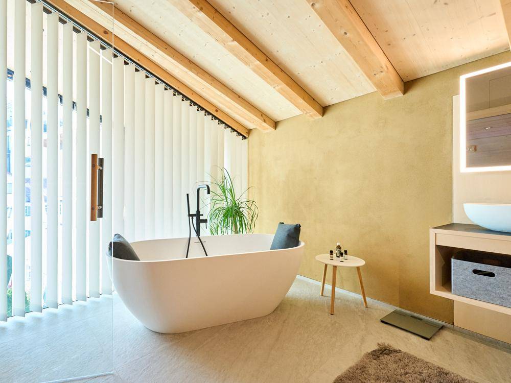 Modernes Badezimmer mit freistehender Badewanne, Holzbalkendecke und vertikalen Jalousien.