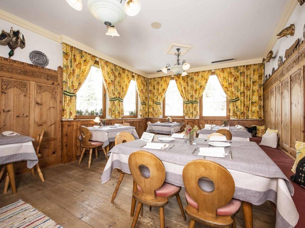 Traditioneller Speisesaal mit Holzböden, holzgetäfelten Wänden und gelben Vorhängen, eingerichtet mit Holztischen und Stühlen.