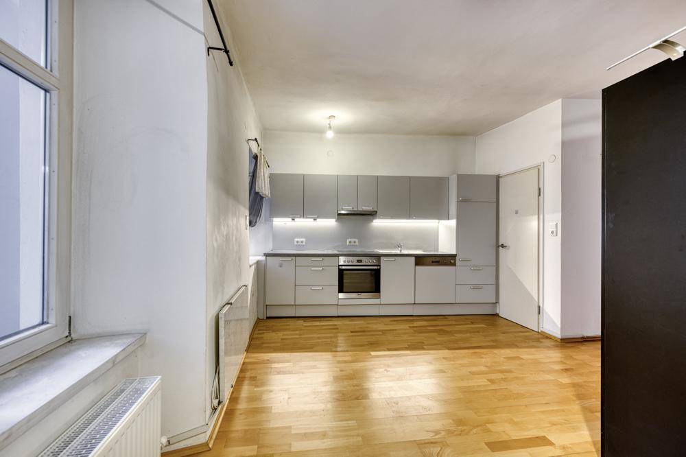 Heller Wohnbereich mit integrierter Küchenzeile, Holzfußboden und großem Fenster.