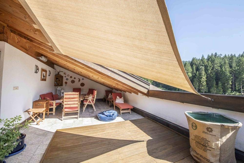 Überdachte Dachterrasse mit Sitzgelegenheiten und Holzboden, umgeben von einer grünen Waldlandschaft.