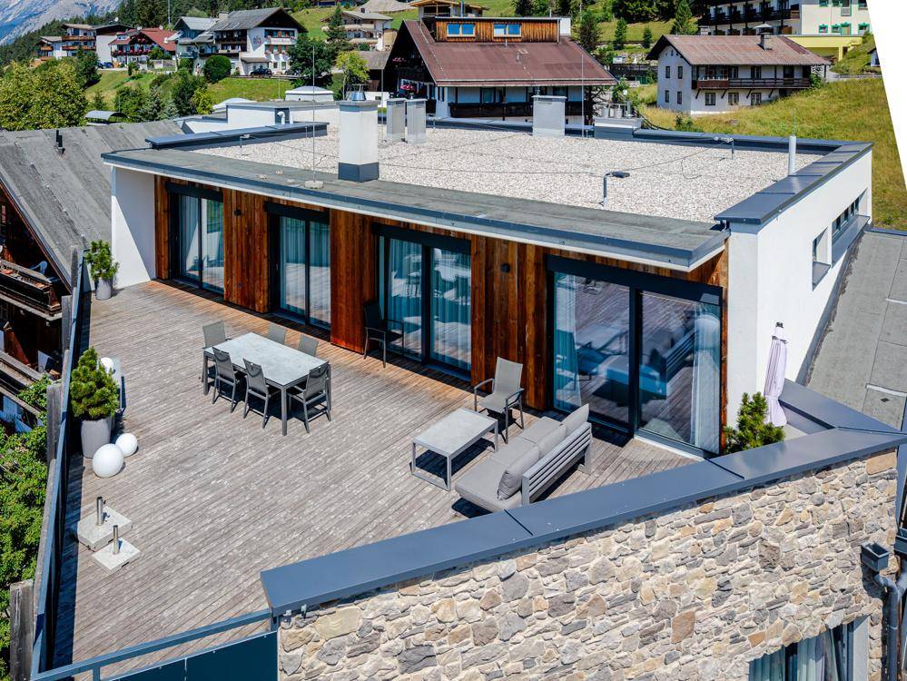 Große Dachterrasse mit Holzbelag und modernen Gartenmöbeln, umgeben von alpiner Landschaft.