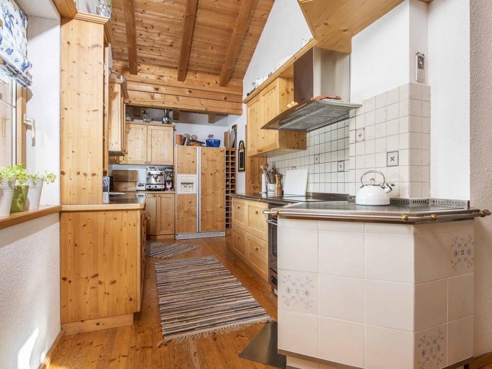 Rustikale Küche mit Holzeinbauschränken, Holzfußboden und einem traditionellen Kachelofen als Kochstelle.