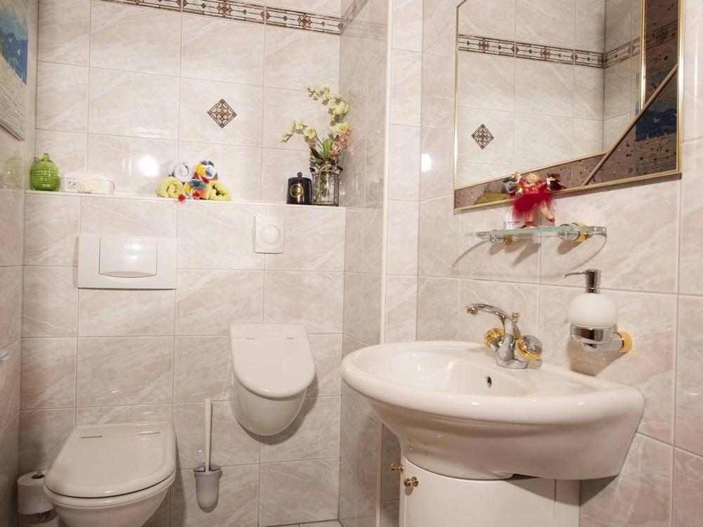 Kleines Gäste-WC mit hellen Fliesen, wandhängender Toilette und einem Waschbecken.