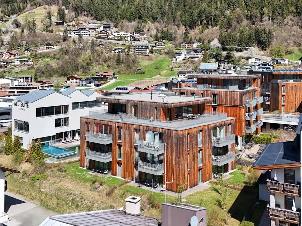Luftaufnahme moderner Gebäude mit Holzfassaden und Balkonen in einer bergigen Landschaft.