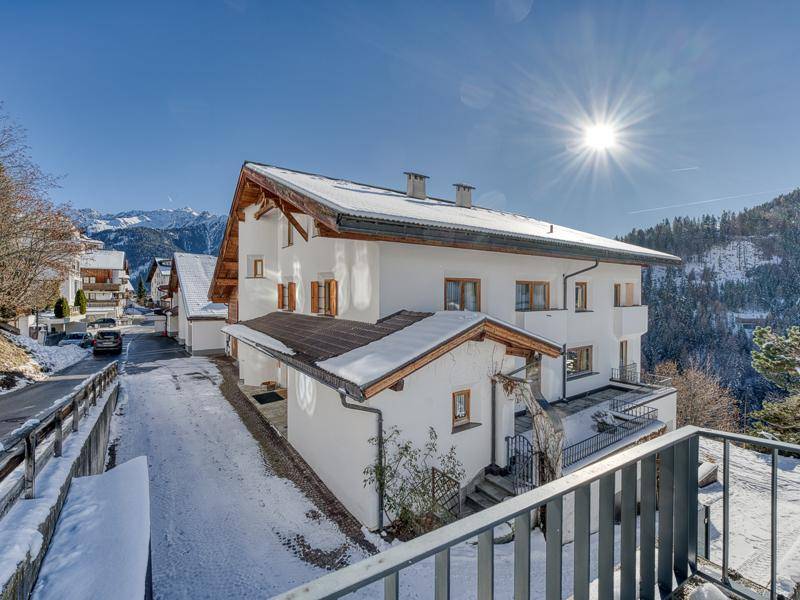Sonnenbeschienenes Chalet mit schneebedecktem Dach und Blick auf die umliegende Berglandschaft.