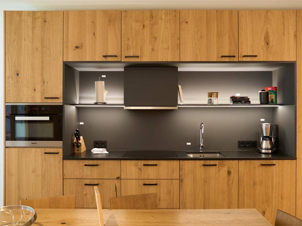 Moderne Einbauküche mit Holzfronten, integrierten Geräten und dunkler Arbeitsplatte.