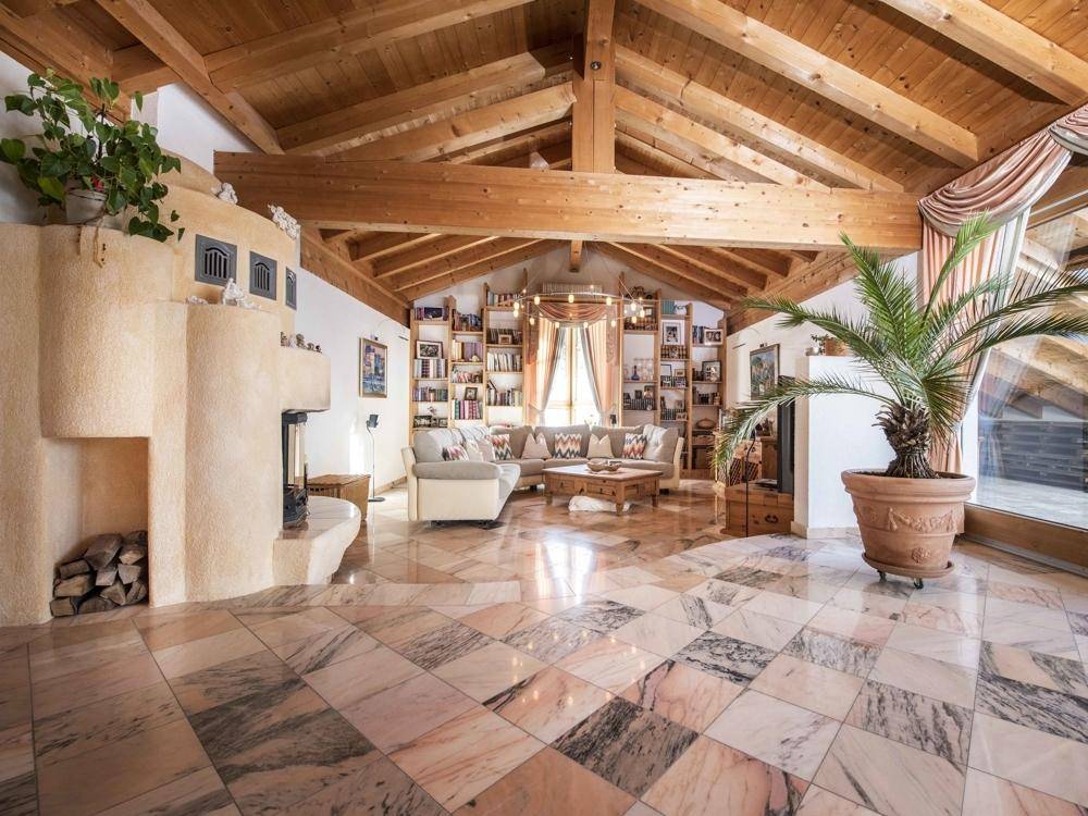 Großzügiges Wohnzimmer mit Marmorboden, offenem Kamin und sichtbaren Holzbalken unter einem hohen Dach.