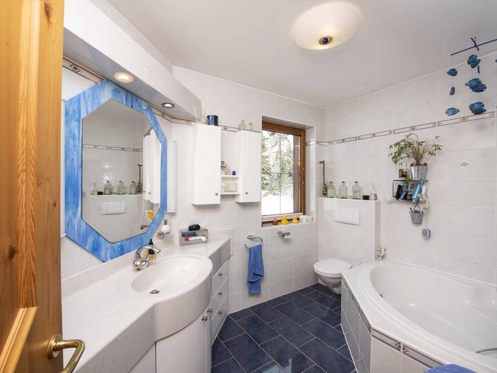 Helles Badezimmer mit blauen Fliesen, Badewanne, Waschbecken und einem Fenster mit Blick nach draußen.