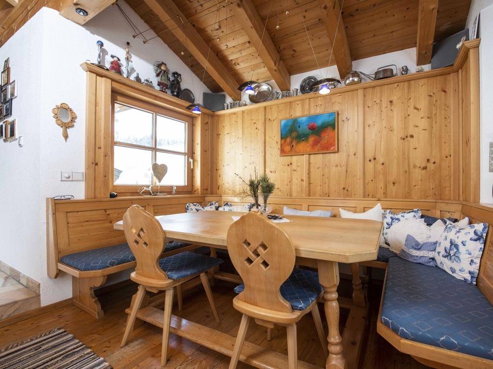 Gemütlicher Essbereich mit Holzbänken und -tisch, umgeben von holzgetäfelten Wänden und einem Fenster.