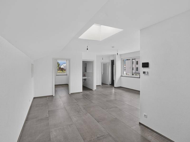 Heller, leerer Raum mit modernen grauen Fliesen, weißen Wänden und einem Oberlicht für viel Tageslicht.