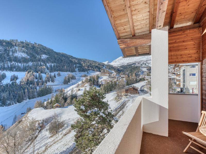 Sonniger Balkon mit Holzboden und atemberaubendem Panoramablick auf die schneebedeckten Berge.