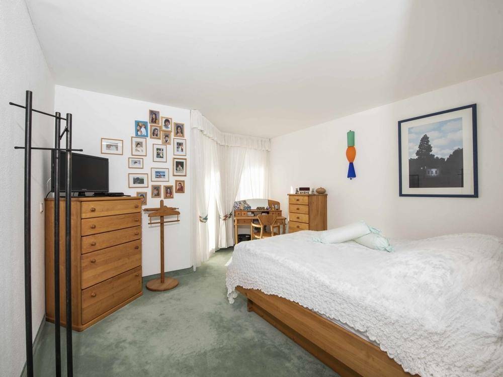 Helles Schlafzimmer mit grünem Teppichboden, Holzmöbeln und einem großen Fenster mit Vorhängen.