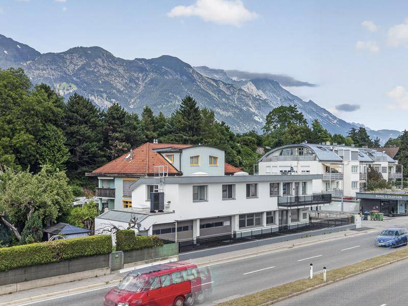 Weitläufige Ansicht des modernen Gebäudes an der Straße, eingebettet in eine grüne Landschaft mit majestätischen Bergen.