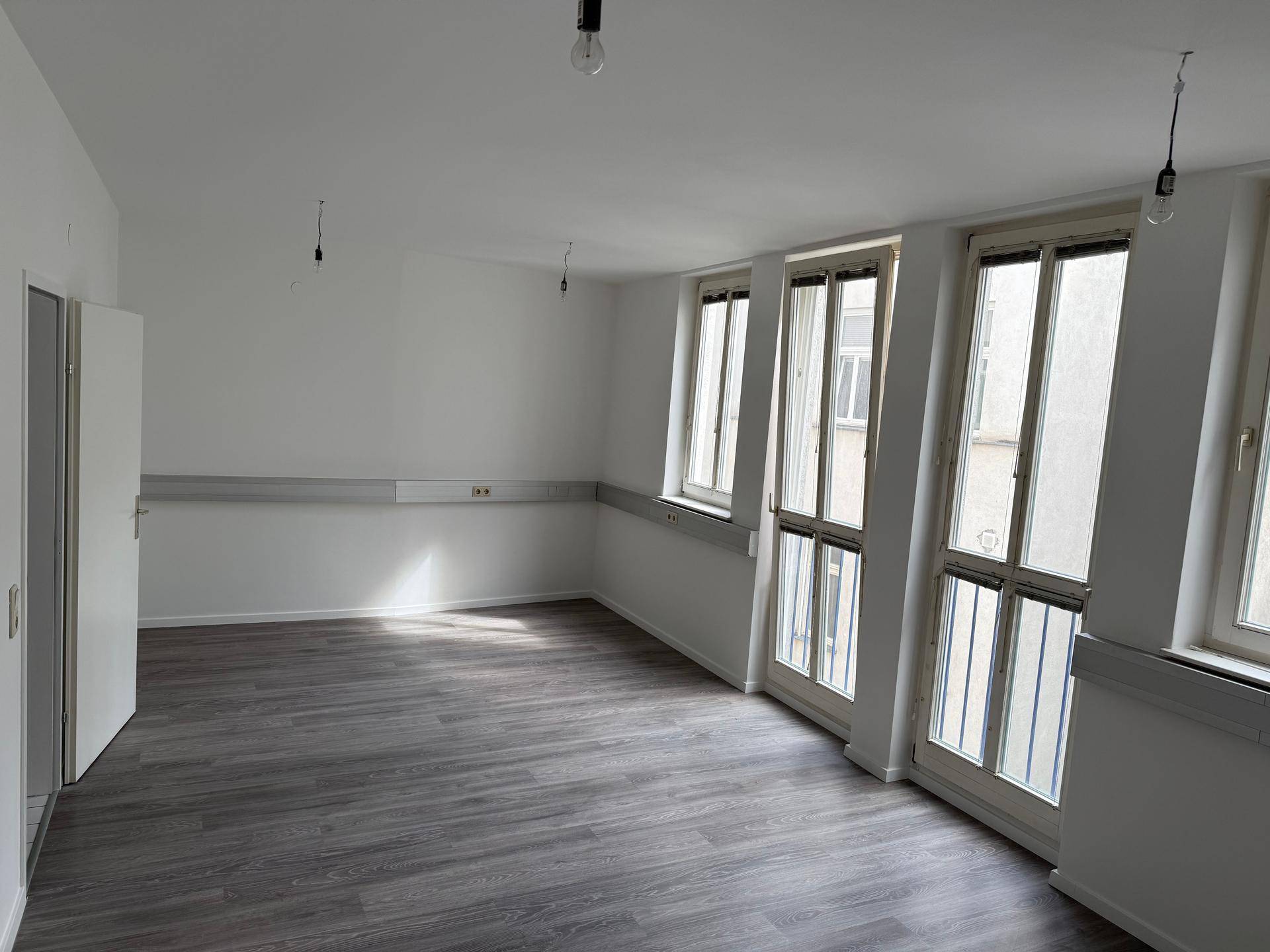 Geräumiger Raum mit Laminatboden und mehreren großen Fenstern, die viel Tageslicht hereinlassen.