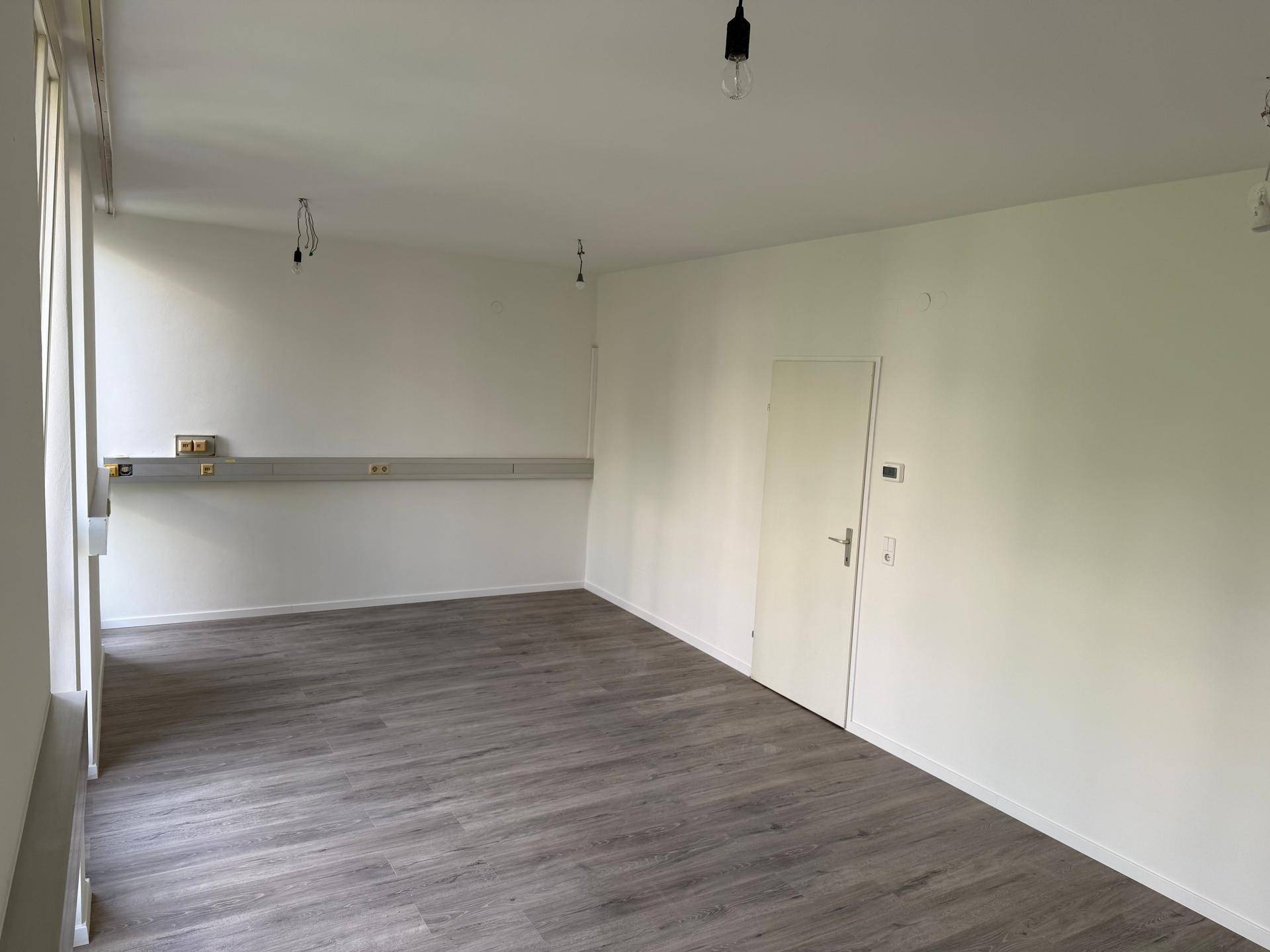 Geräumiger Raum mit Laminatboden und weißen Wänden, ausgestattet mit einer Tür und Fensterfront.