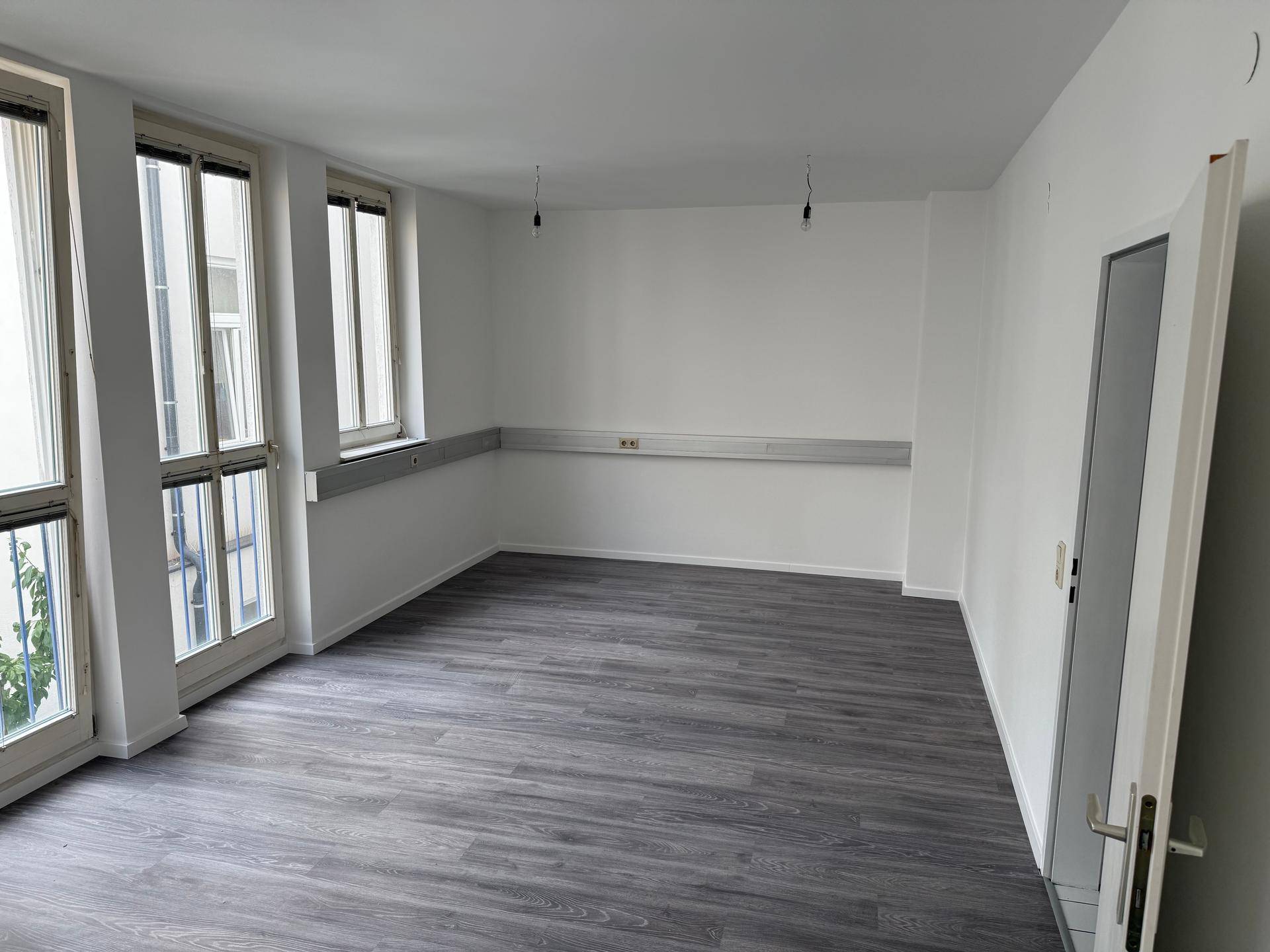Heller Raum mit Laminatboden und großen Fenstern, die einen Blick nach draußen ermöglichen.