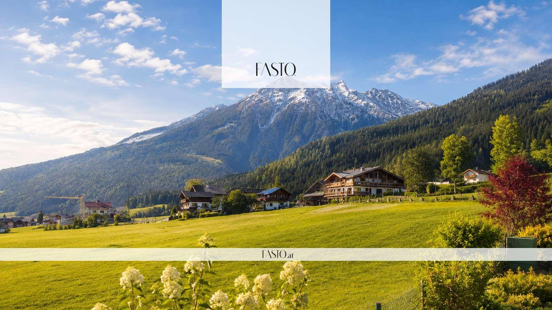 Weitläufige Landschaft mit grünen Wiesen, traditionellen Häusern und schneebedeckten Bergen im Hintergrund.