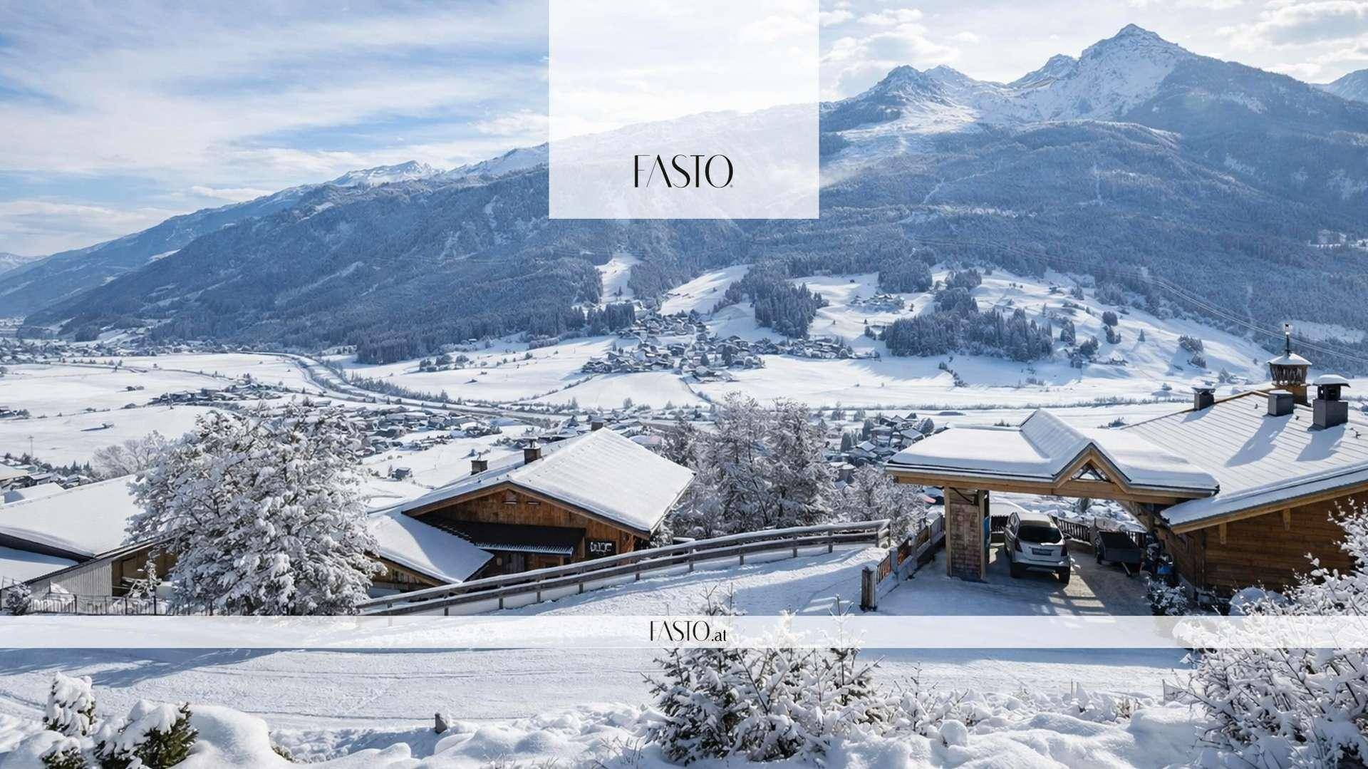 Winterliche Ansicht eines verschneiten Dorfes in einem Tal, umgeben von schneebedeckten Bergen und Wäldern.