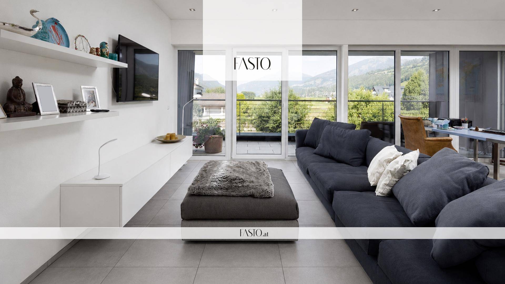 Modernes Wohnzimmer mit großem Sofa, Fliesenboden und Zugang zu einem Balkon mit Bergblick.