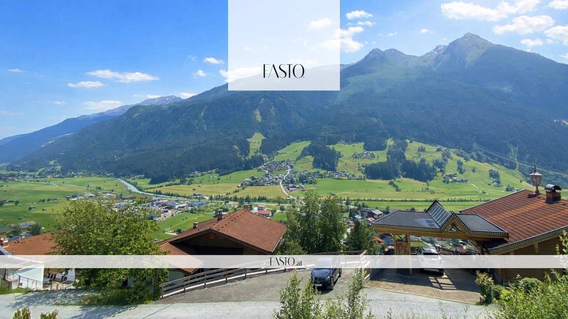 Weitläufiger Ausblick über ein Tal mit einer Ortschaft und imposanten Bergen im Hintergrund.