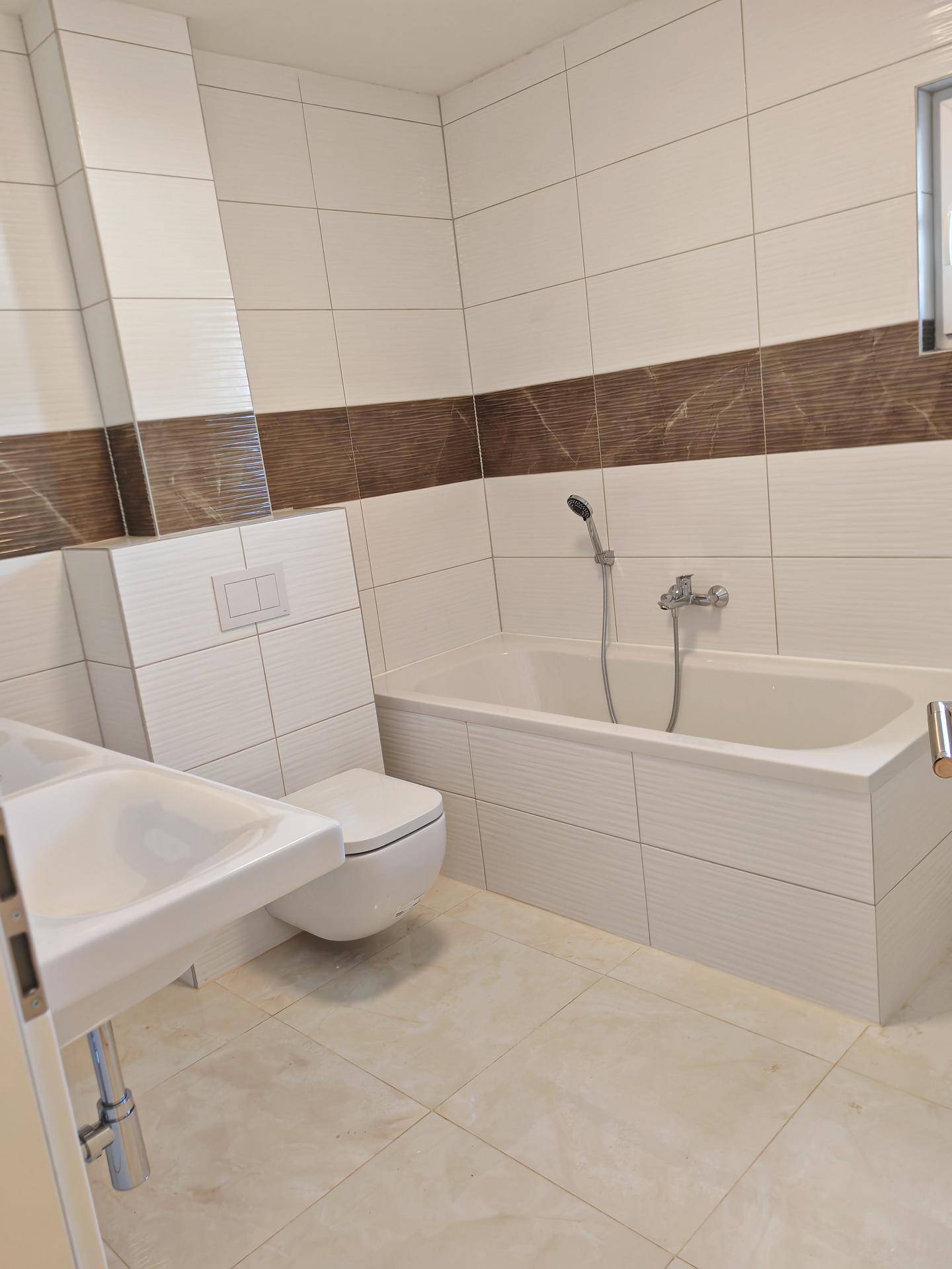 Helles Badezimmer mit Badewanne, Waschbecken und Wand-WC, modern gefliest.