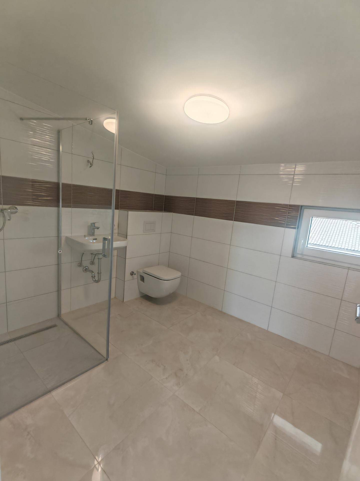 Modernes Badezimmer mit Dusche, Wand-WC und Fenster, hell gefliest in Weiß und Braun.