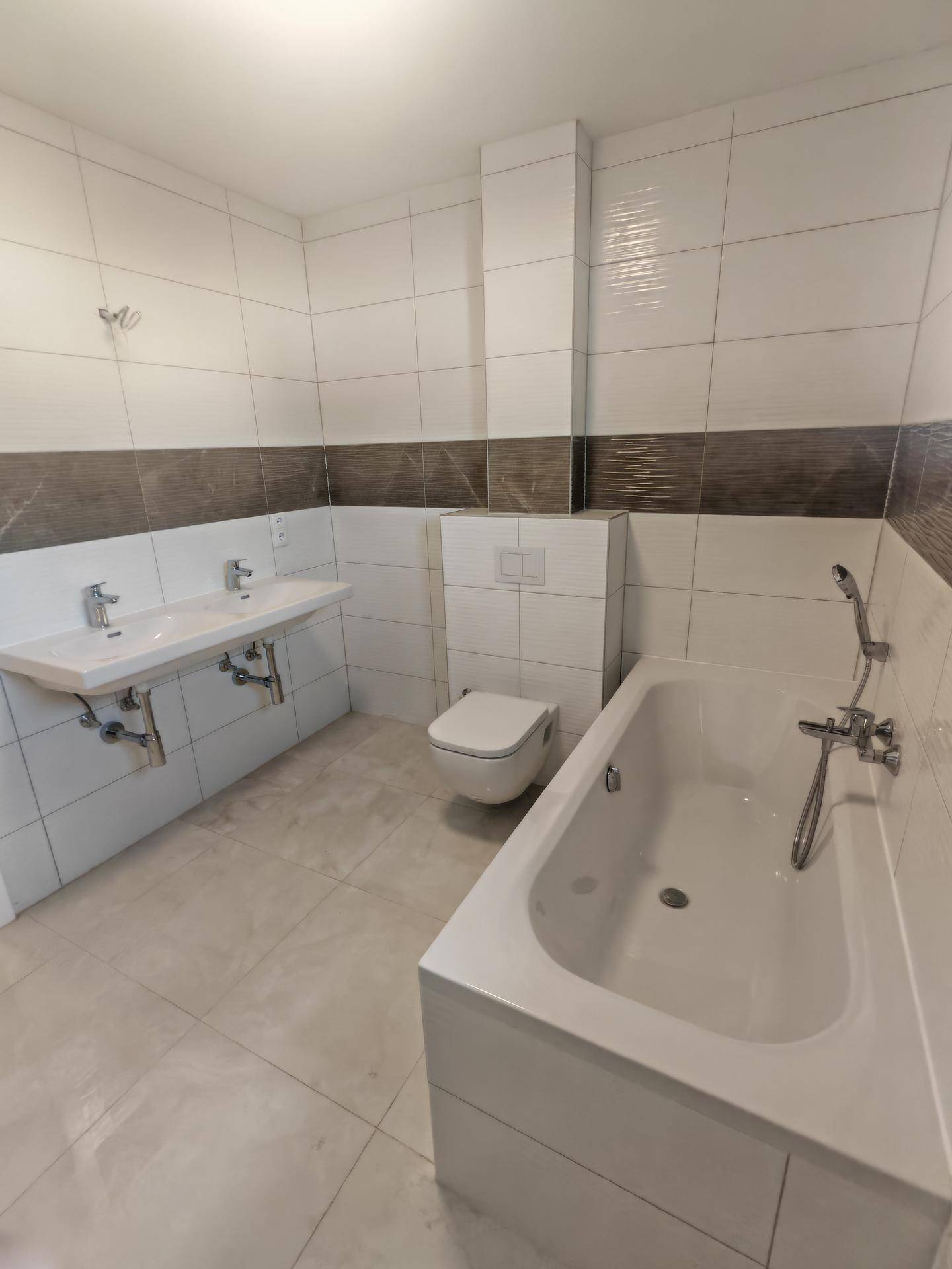 Modernes Badezimmer mit Badewanne, Doppelwaschbecken und Wand-WC, hell gefliest.