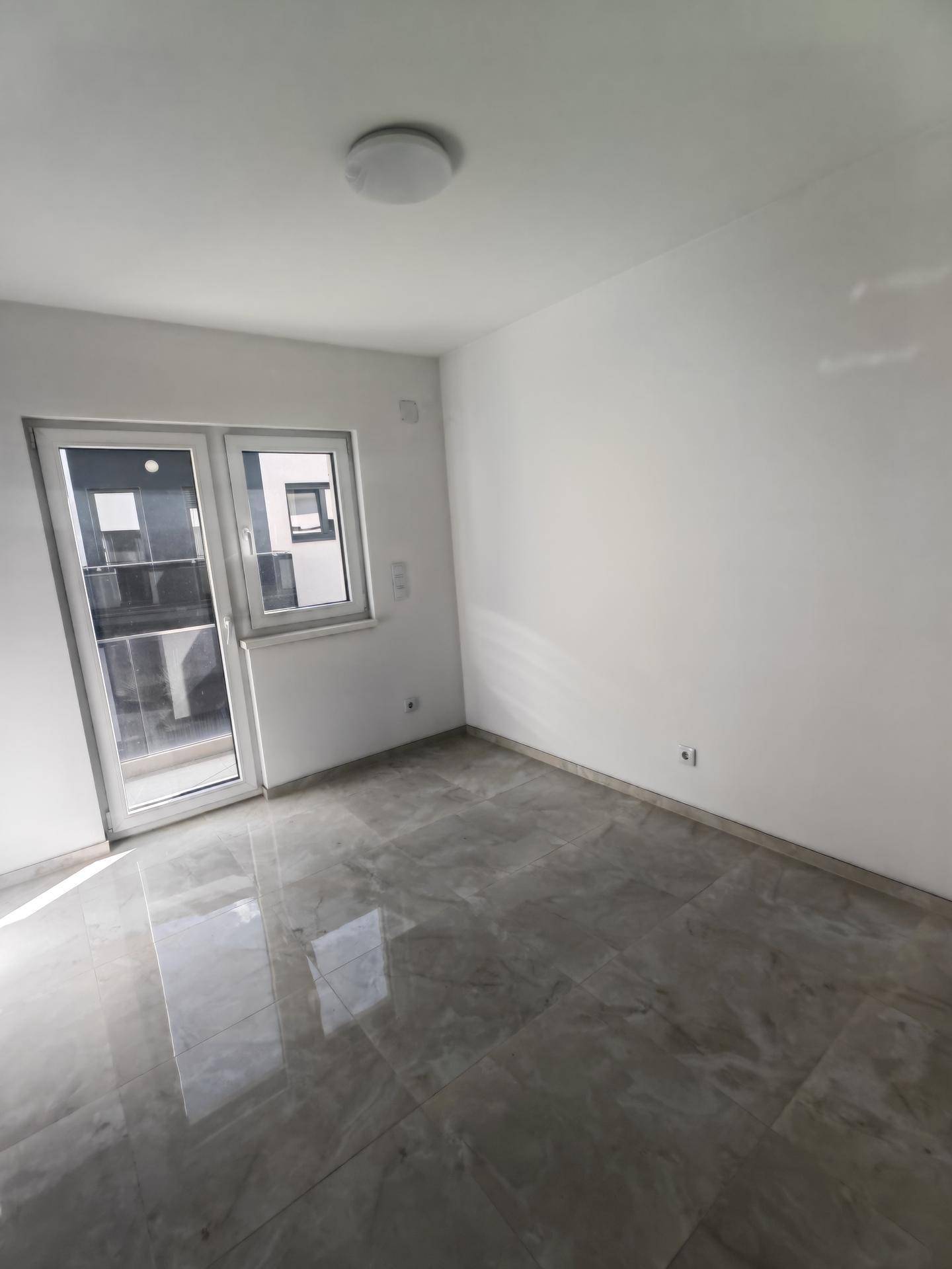 Helles Schlafzimmer mit Fliesenboden und Zugang zu einem Außenbereich, viel Tageslicht.