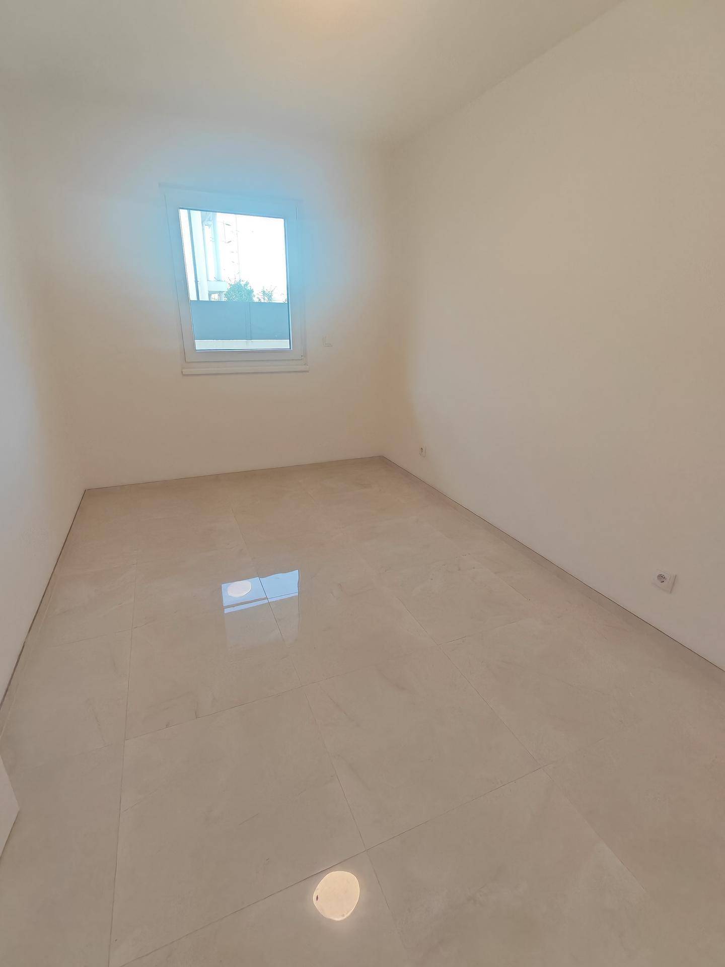 Leeres Schlafzimmer mit Fliesenboden und Fenster, bereit zur individuellen Einrichtung.