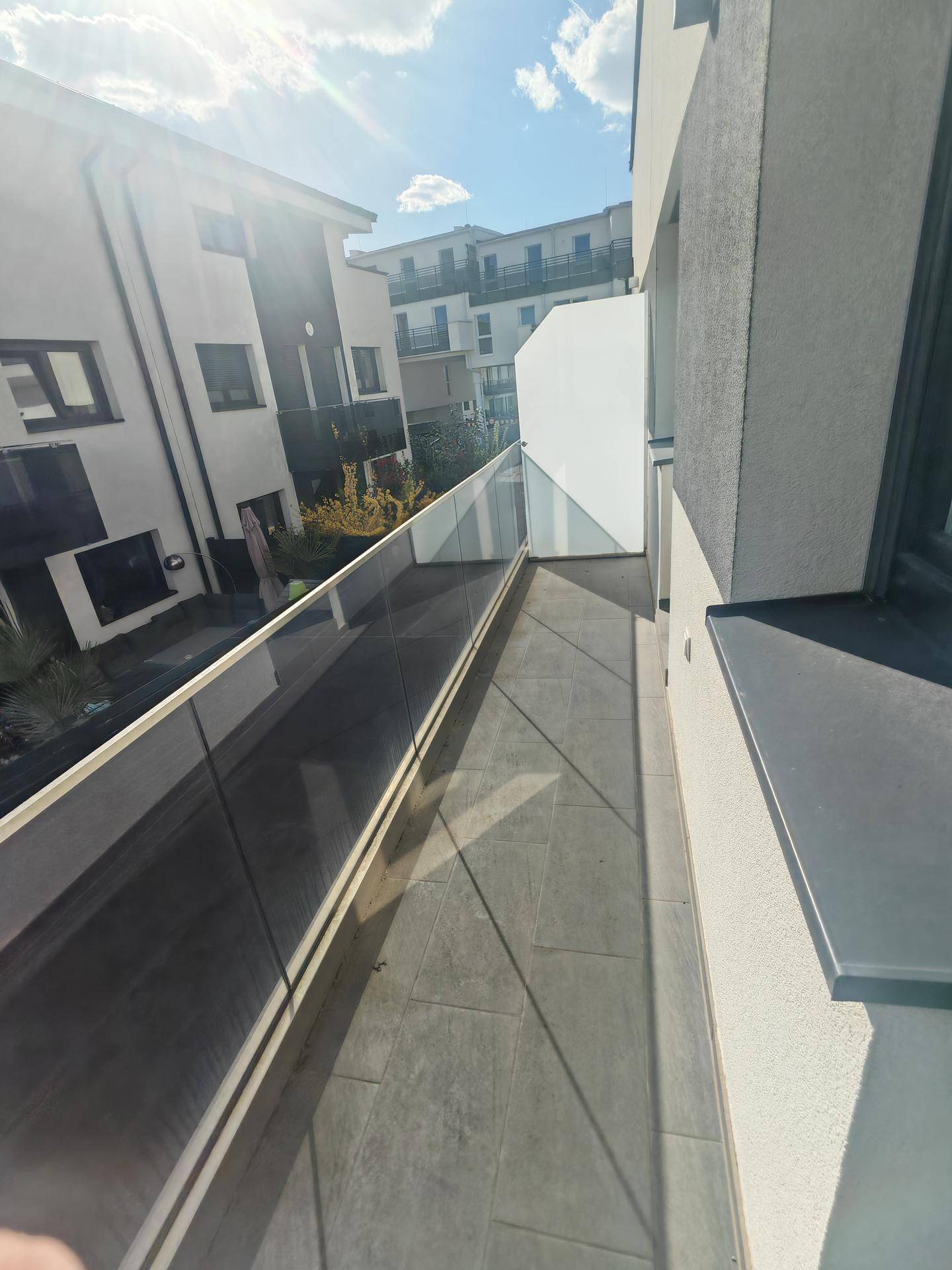 Langer Balkon mit Glasgeländer und Fliesenboden, sonnig und modern gestaltet.