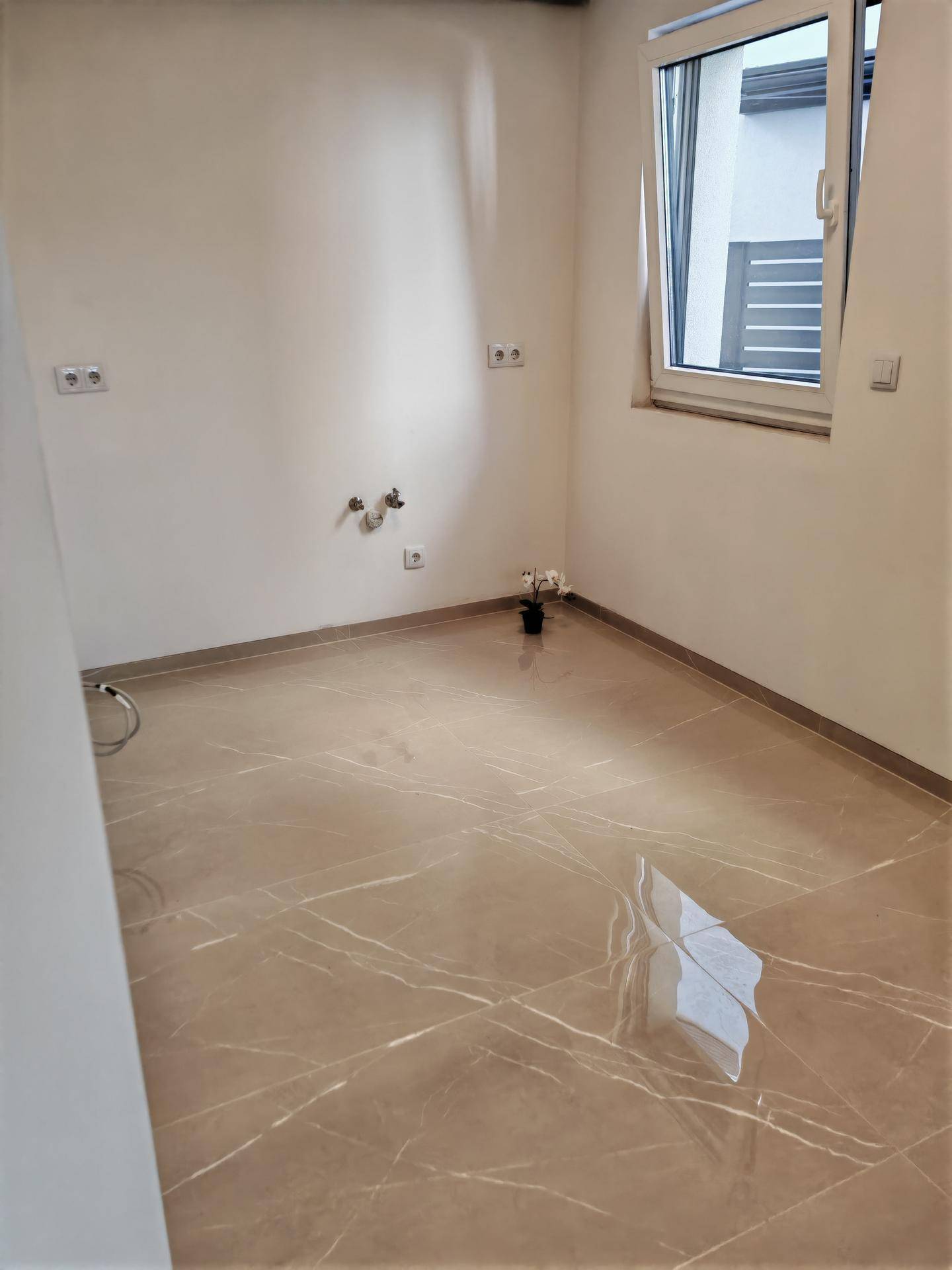 Leerer Raum mit Fliesenboden und Anschlüssen für Waschmaschine oder Spüle, bereit zur Nutzung.