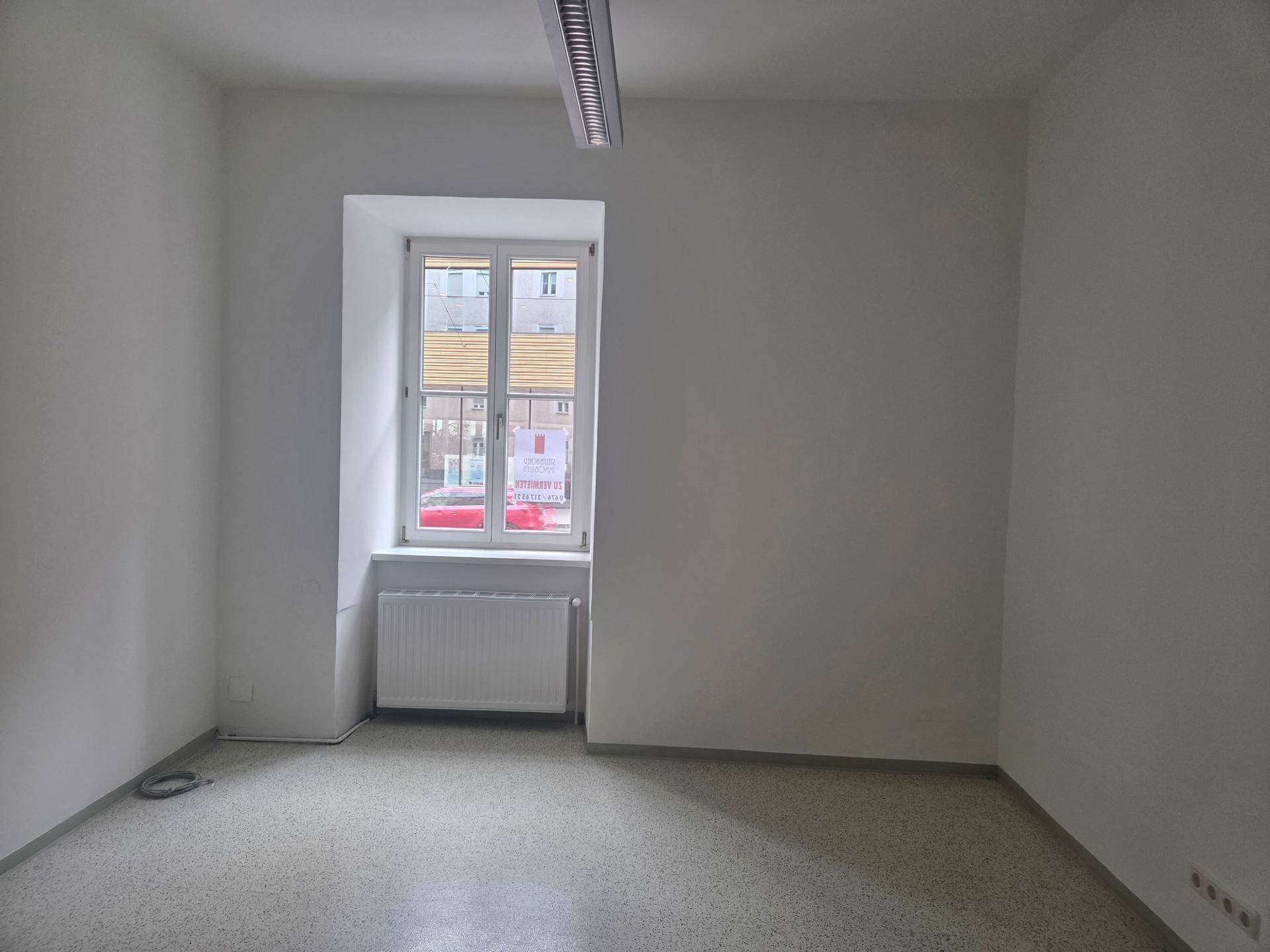 Leerer Raum mit weiß gestrichenen Wänden, einem Fenster und einem Heizkörper, bereit zur Nutzung.