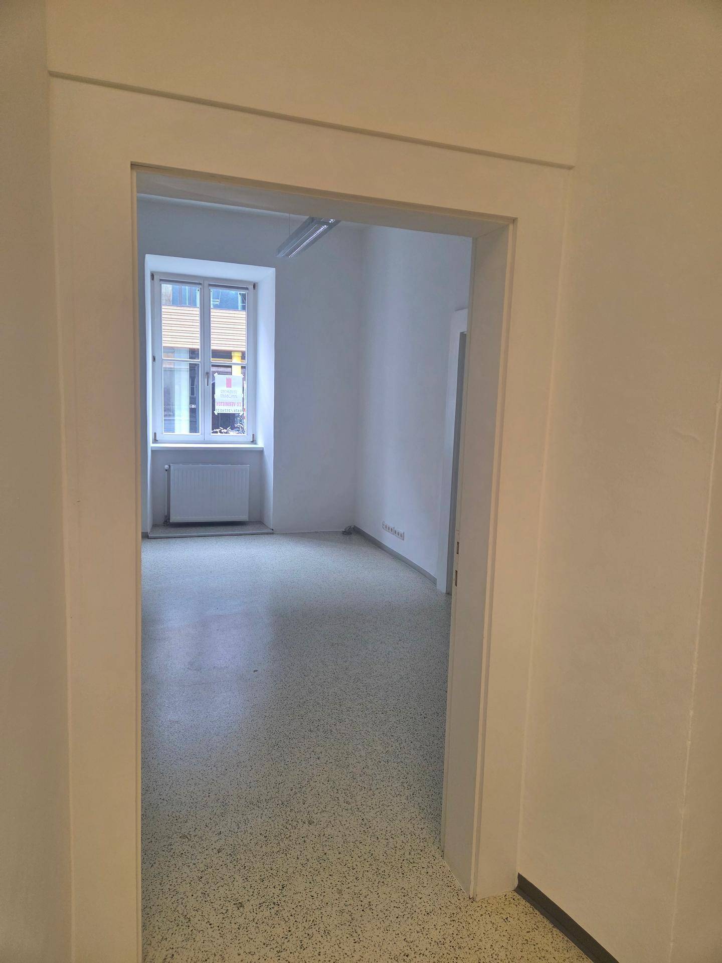 Blick durch einen Türrahmen in einen hellen, leeren Raum mit einem Fenster und Vinylboden.
